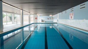 Una gran piscina interior con agua cristalina, paredes enlosadas y un techo con diseños lineales.