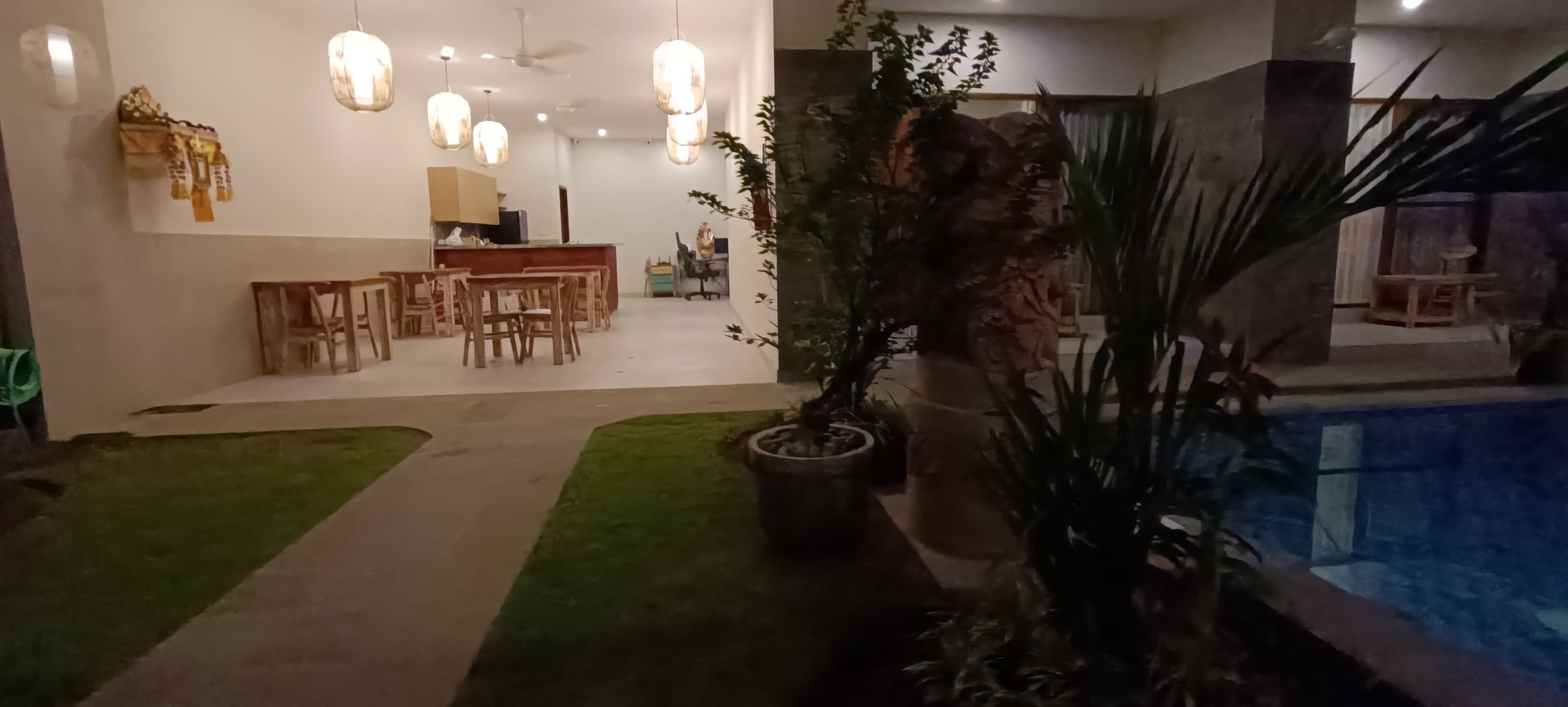 A modern indoor pool area with a dining area and a kitchen in the background.
