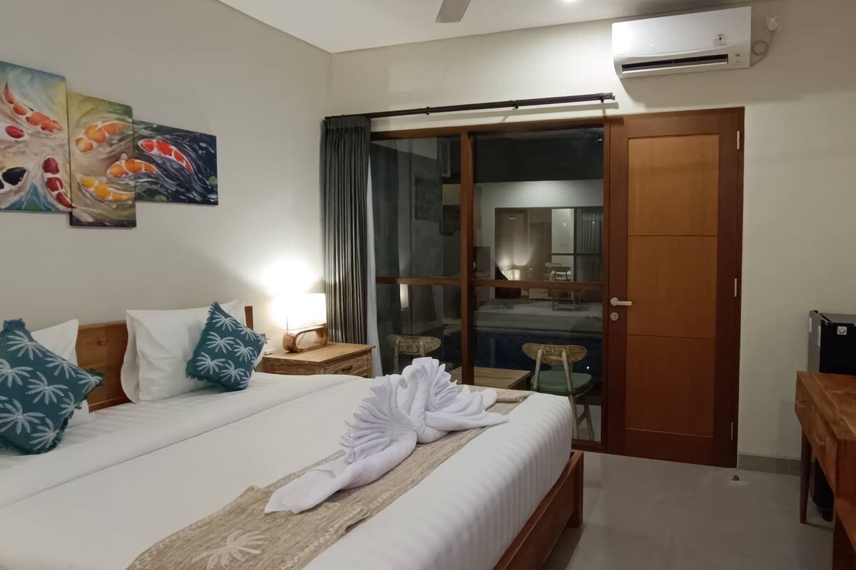 A hotel room with a bed, a TV, a painting, and a sliding door to a balcony.