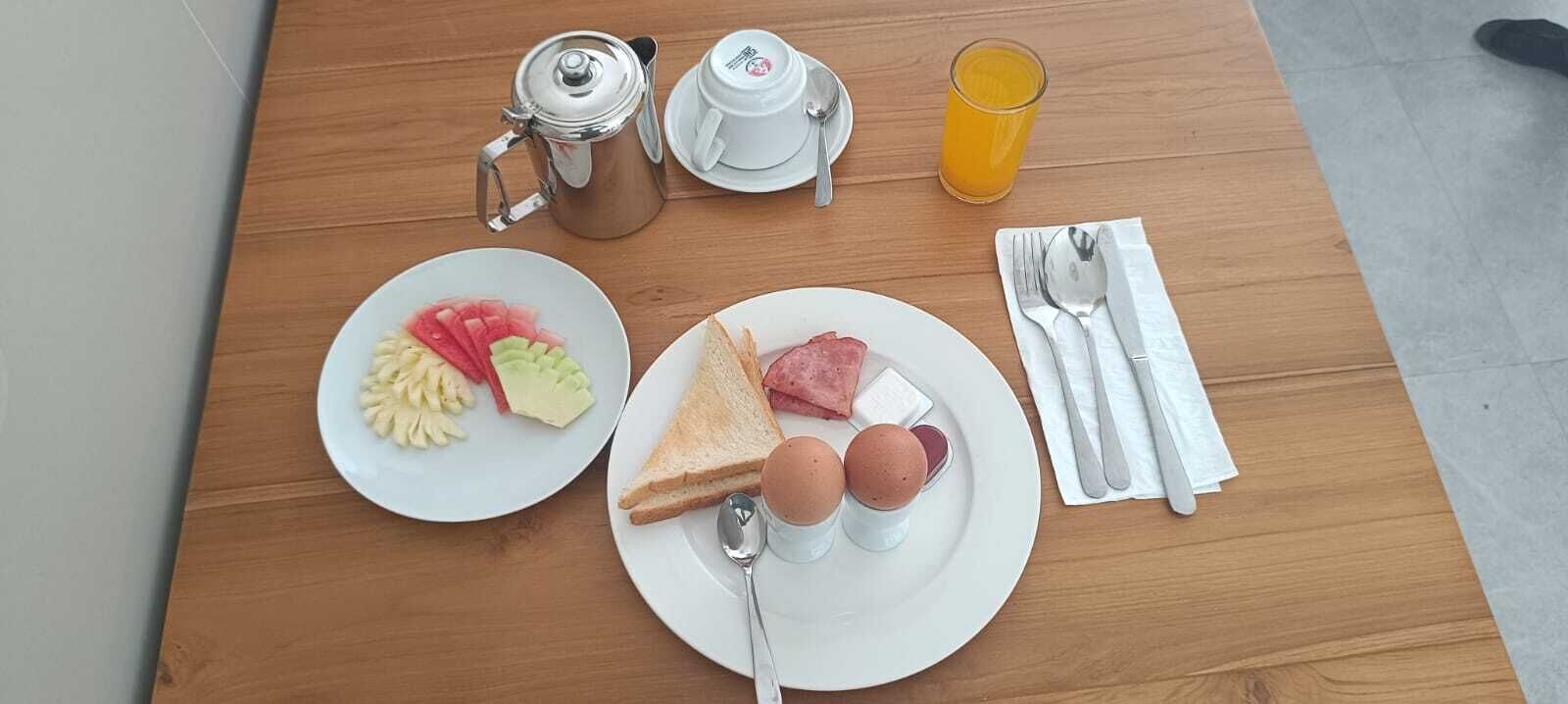 A breakfast setup with a coffee pot, a glass of orange juice, two plates with eggs, toast, and sliced fruit on a wooden table.