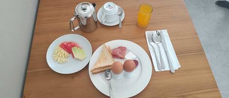 A breakfast setup with a coffee pot, a glass of orange juice, two plates with eggs, toast, and sliced fruit on a wooden table.