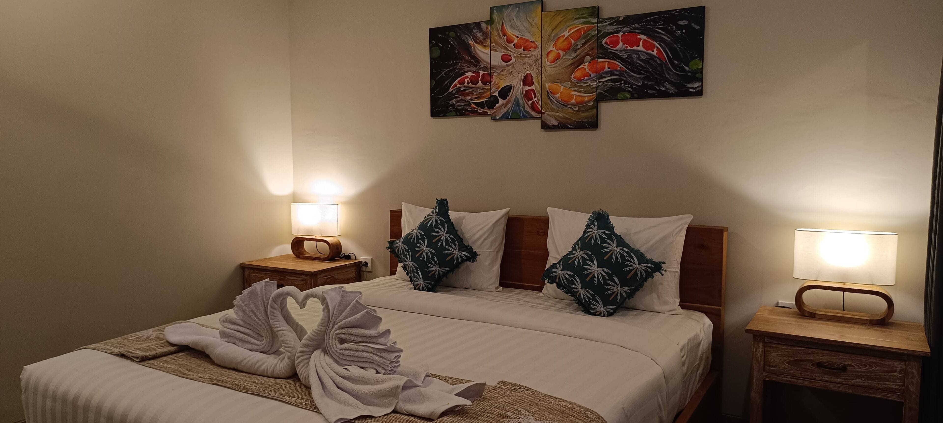 Quarto de hotel com uma cama grande, duas mesas de cabeceira com abajures e uma parede com três quadros.