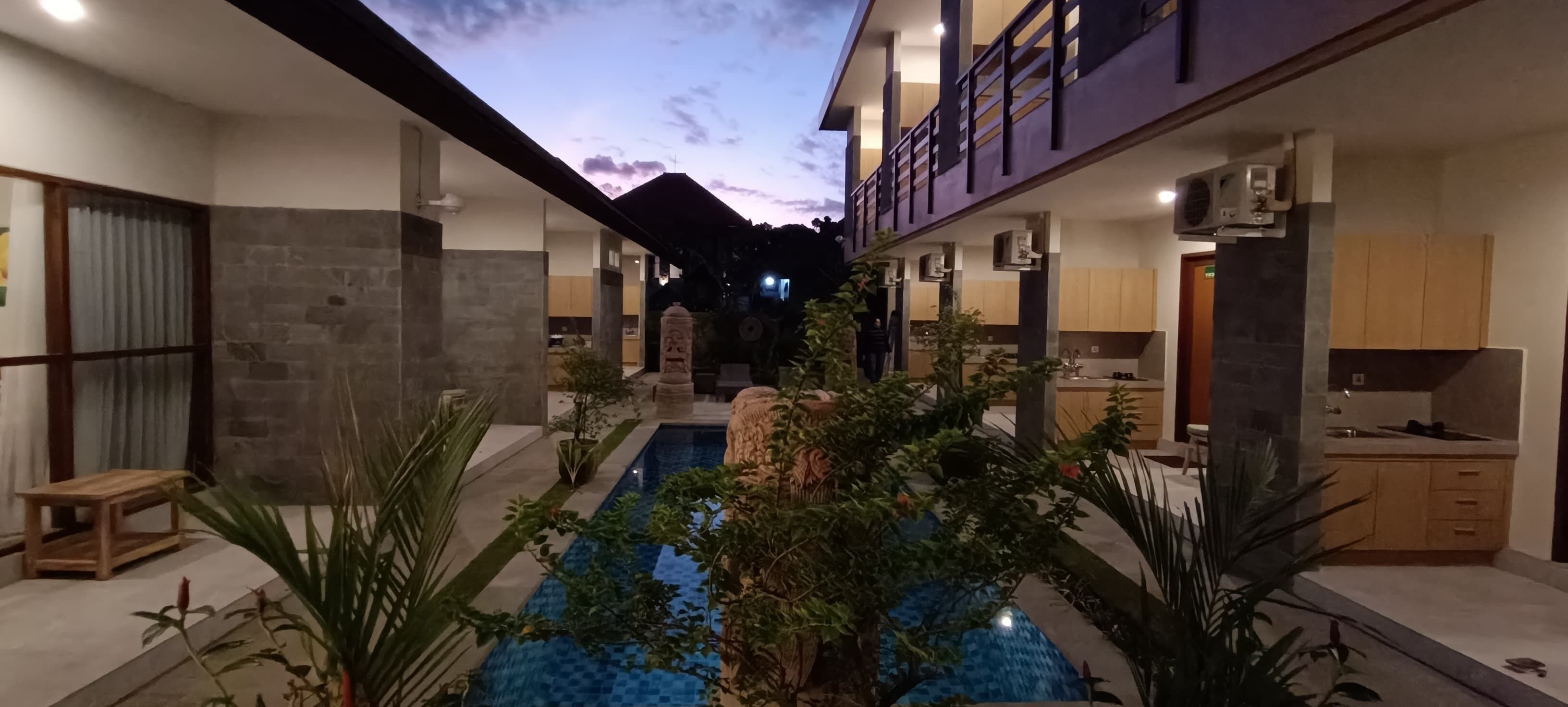 Un hotel moderno con un patio central que cuenta con una piscina, rodeado por habitaciones con paredes de piedra y mobiliario de madera.