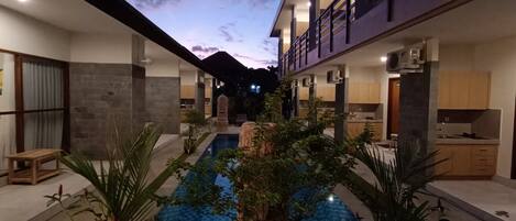 Un hotel moderno con un patio central que cuenta con una piscina, rodeado por habitaciones con paredes de piedra y mobiliario de madera.