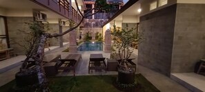Un área de piscina moderna al aire libre con un muro de piedra, bancos de madera y plantas en macetas.