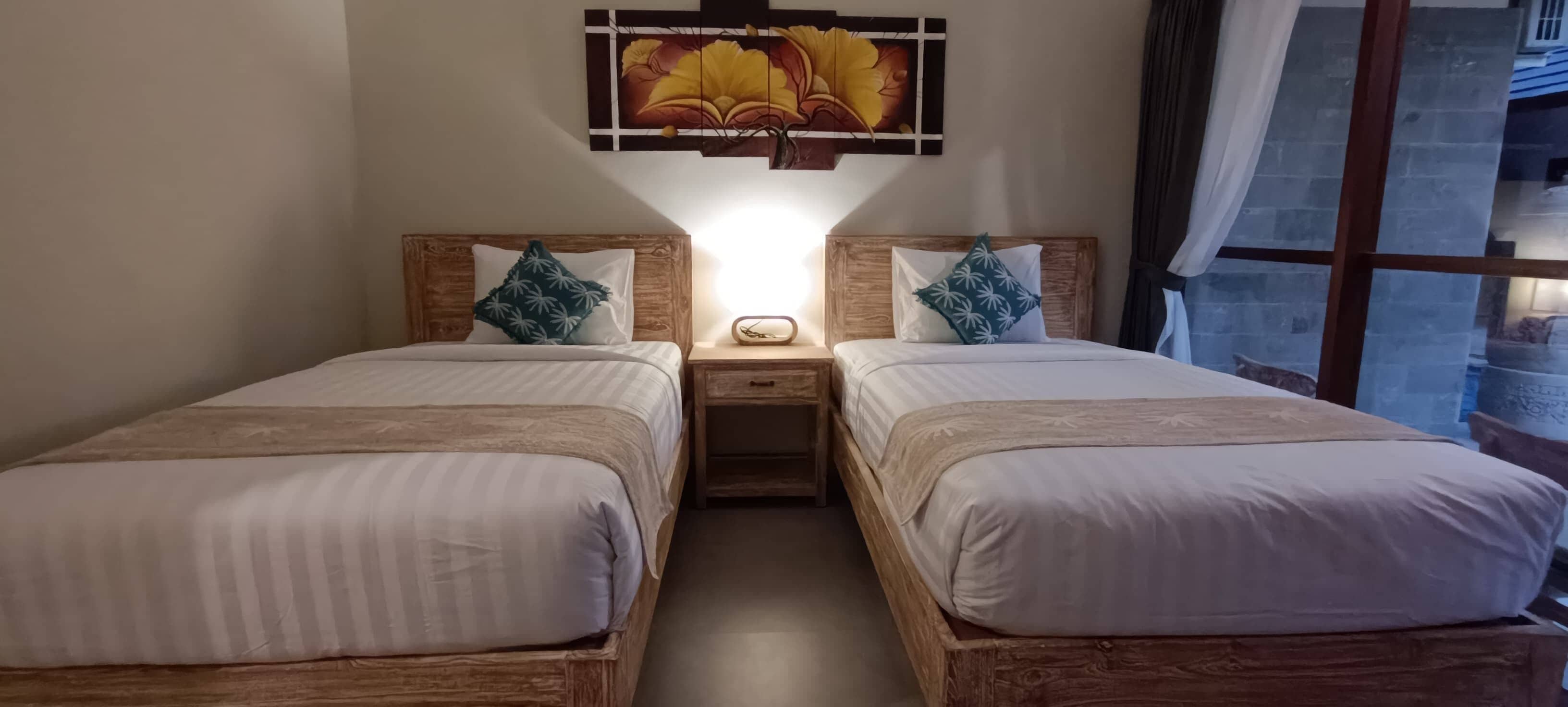 A double bed room with wooden headboards, a nightstand, and a wall-mounted artwork.