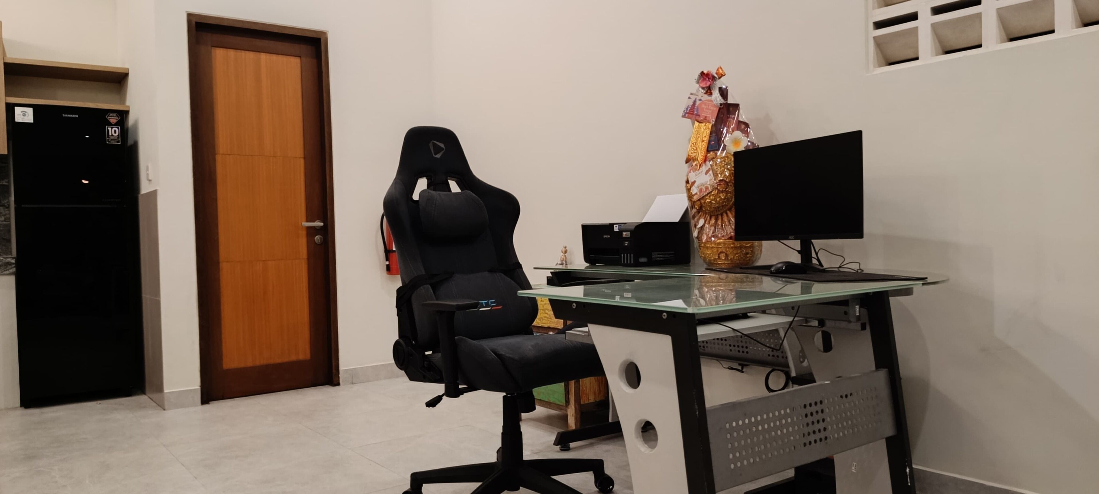 A home office setup with a gaming chair, a desk, a computer monitor, and a decorative vase.