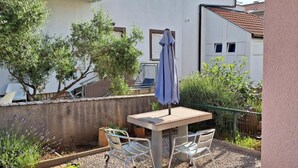 A patio with a table and chairs, a blue umbrella, and a white building with windows in the background.