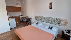 A bedroom with a bed, a small kitchenette, and a dining area.