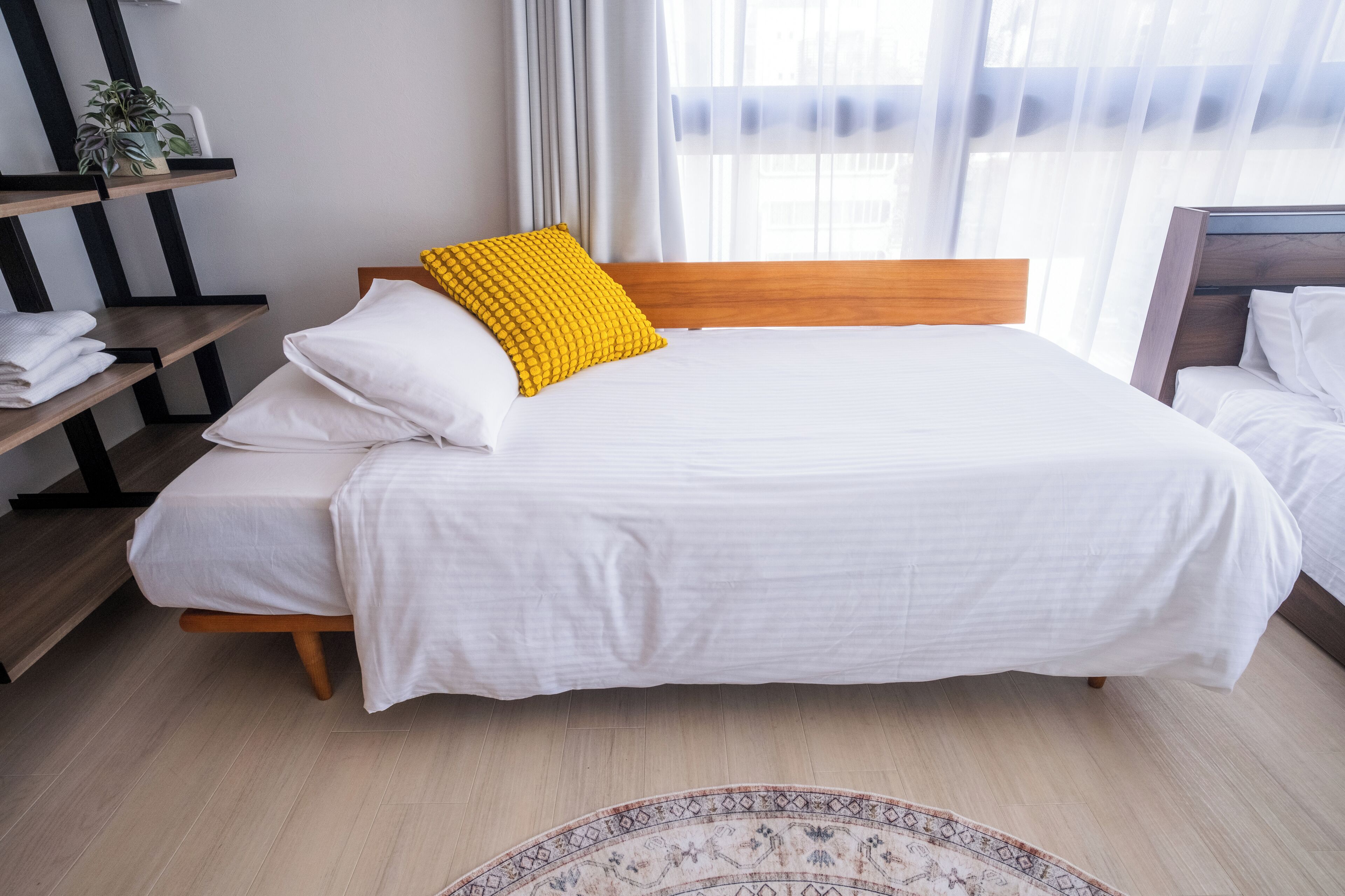 Un letto ben rifatto con lenzuola bianche e un cuscino giallo, una testiera in legno e un comodino con asciugamani piegati.