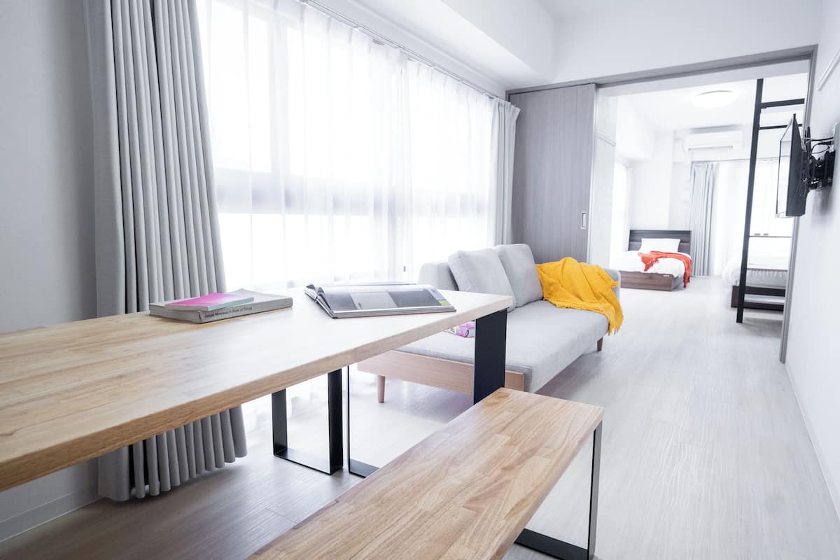 Ein modernes Hotelzimmer mit einem Holztisch, einem Sofa mit gelber Decke und Blick auf das Nachbarzimmer.