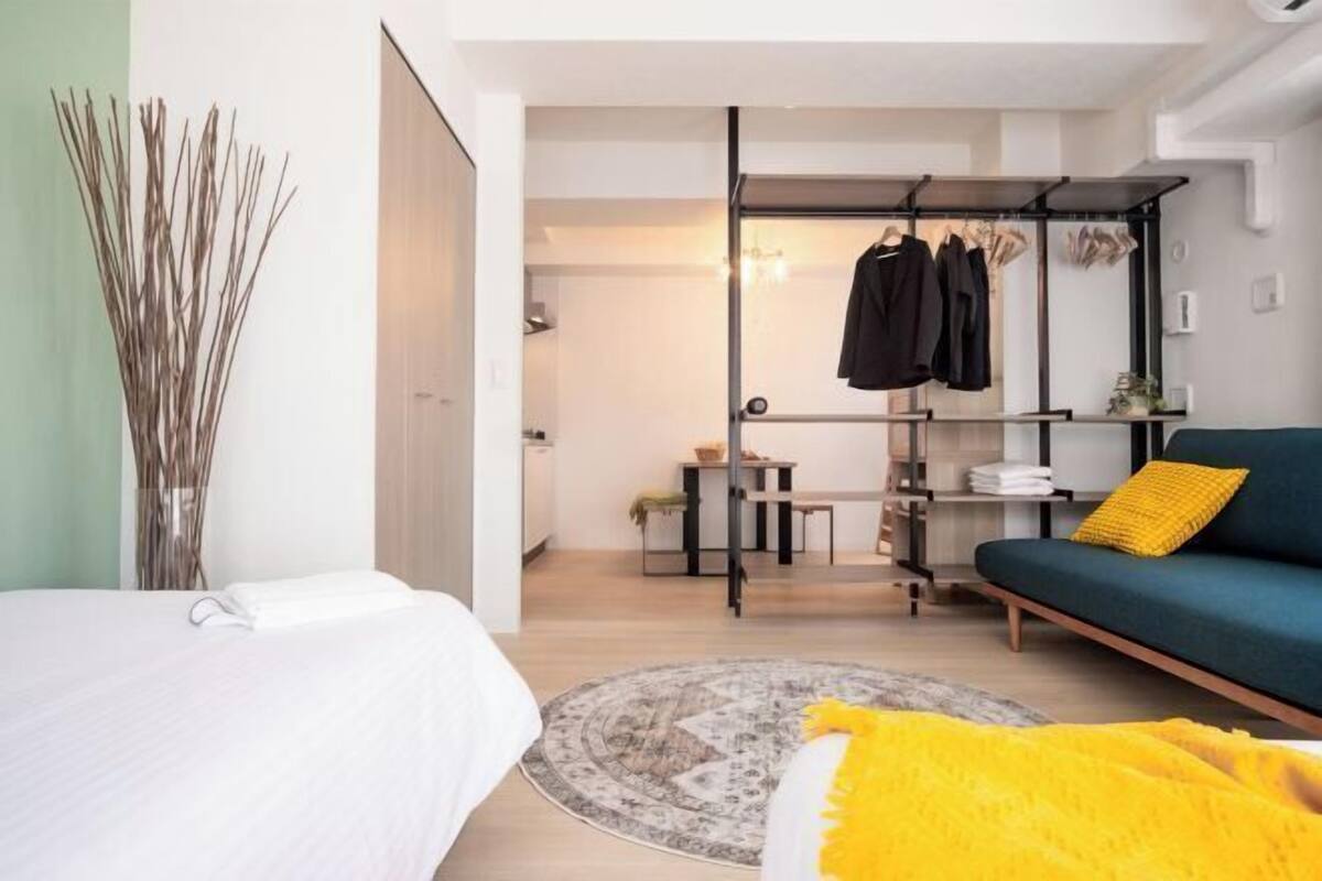 Ein modernes Schlafzimmer mit einem Bett, einem Sofa, einem Kleiderständer und einem kleinen Tisch mit einer Lampe.