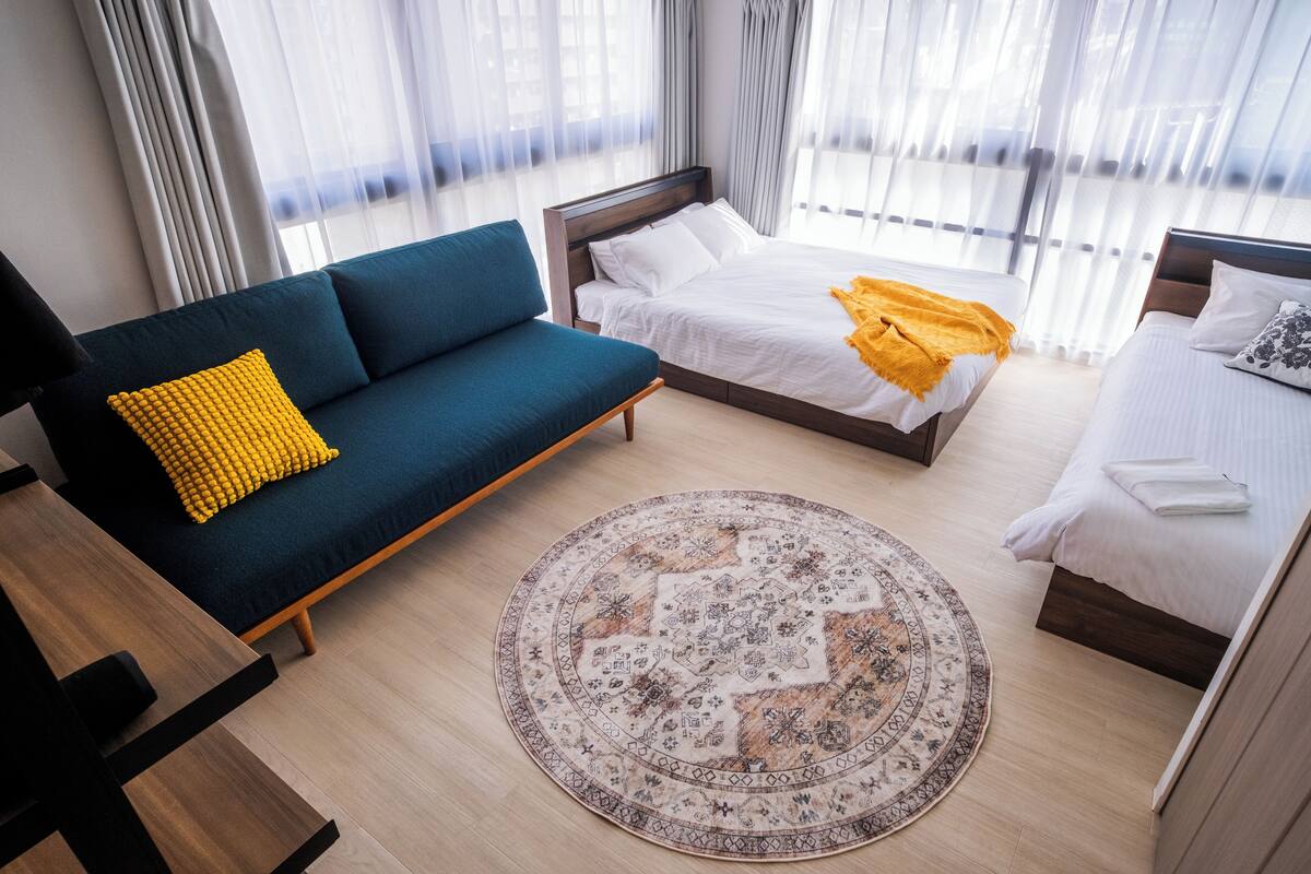 Ein modernes Hotelzimmer mit einem blauen Sofa, einem Doppelbett mit gelber Decke und einem gemusterten Teppich.