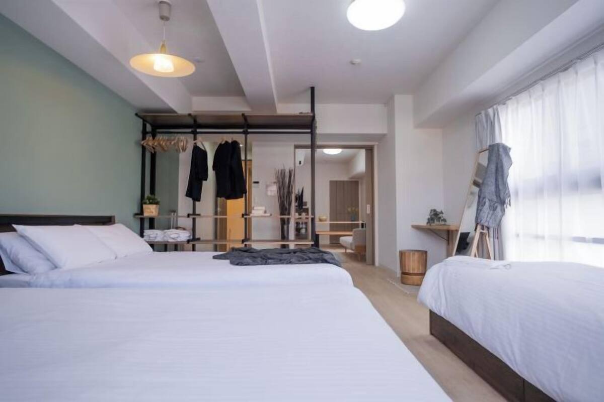 Ein modernes Hotelzimmer mit zwei Betten, einem Schrank, einem Spiegel und einem Fenster mit durchsichtigen Vorhängen.