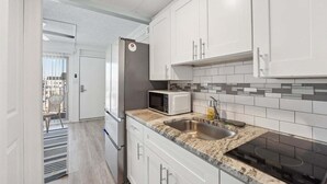 Une cuisine moderne avec des meubles blancs, un réfrigérateur en acier inoxydable, un four à micro-ondes, un évier et une plaque de cuisson noire.