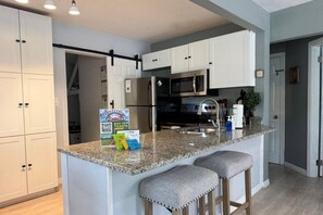 A modern kitchen with white cabinets, a granite countertop, stainless steel appliances, and two bar stools. - Cute and Cozy 2 bedroom bungalow in Seminole Heights (Tampa)