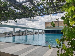 Zwembad met ligbedden en een overdekt gedeelte, omringd door een modern gebouw en groen.