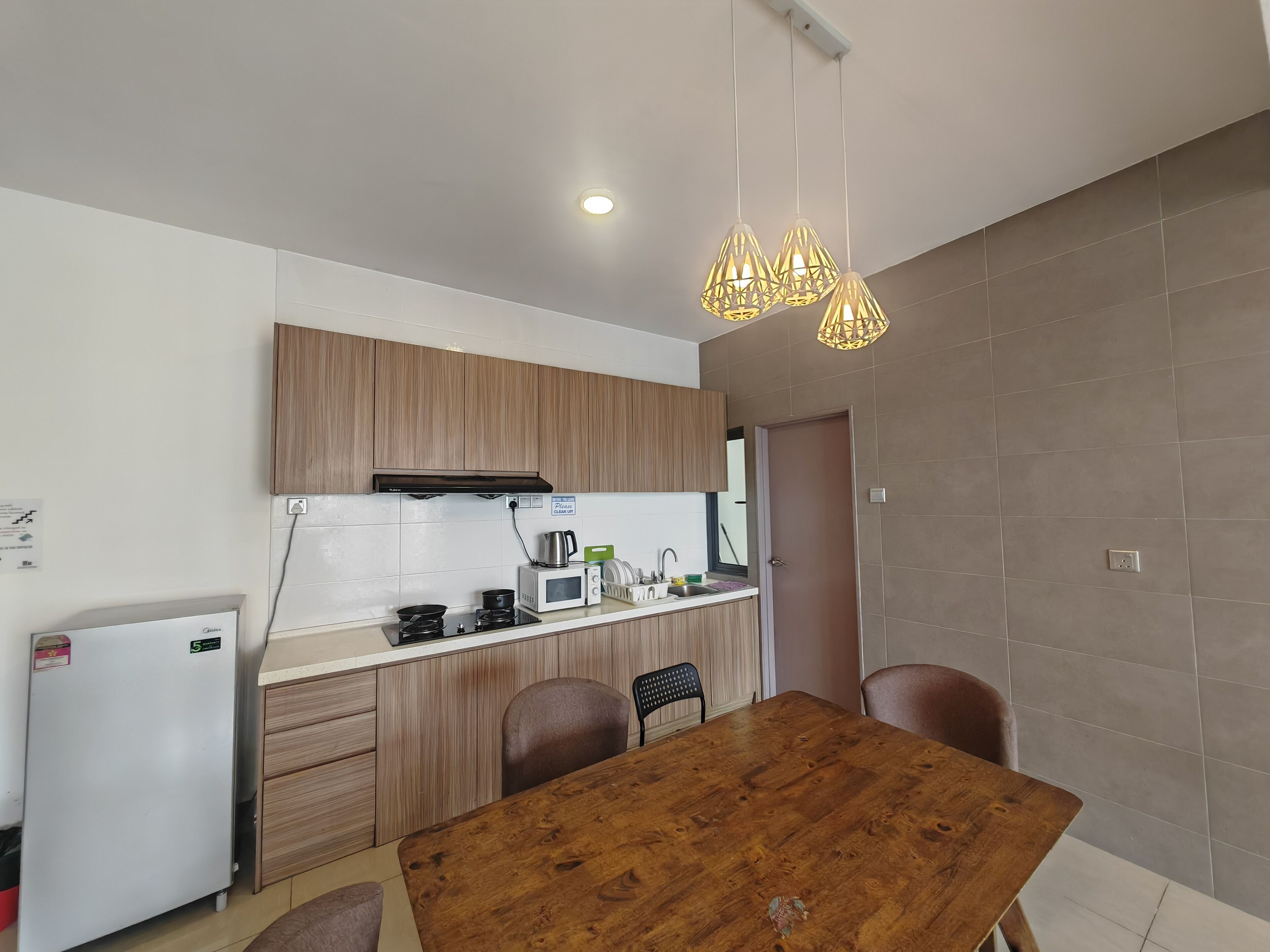 A modern kitchen with wooden cabinets, a built-in microwave, a kettle, and a coffee maker. There is a wooden dining table with chairs.