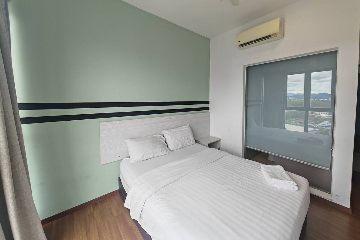 A hotel room with a bed, a nightstand, a window with a view, and an air conditioning unit.