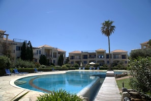 A resort with a swimming pool, lounge chairs, and a palm tree. - Cassiopeia 1BR Apt on Beach with Pool (Pyrgos Psilonerou)