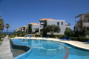 Une piscine dotée d’une terrasse en bois, entourée de chaises longues et offrant une vue dégagée sur la mer.