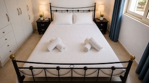Una cama bien hecha con sábanas blancas y dos toallas enrolladas sobre la cama.