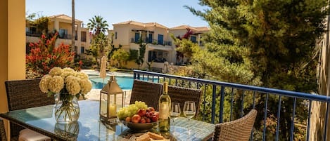 A balcony with a table set for two, featuring a vase of flowers, a bowl of fruit, a bottle of wine, and glasses.