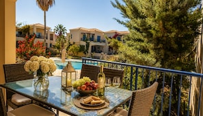 A balcony with a table set for two, featuring a vase of flowers, a bowl of fruit, a bottle of wine, and glasses. - Cassiopeia 1BR Apt on Beach with Pool (Pyrgos Psilonerou)