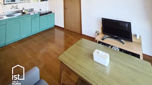 A modern kitchen with teal cabinets, a wooden dining table, and a TV on a wooden stand. - Designer Island Villa with Stunning Panoramic Sea Views (Bizen)