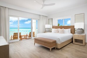 Een ruime slaapkamer met een groot bed, een houten bankje, een nachtkastje en uitzicht op de oceaan.