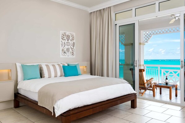 Een slaapkamer met een bed, nachtkastje, decoratieve wanddecoratie en een balkon met uitzicht op de oceaan.