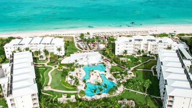 Luchtbeeld van een resort met een centraal gelegen zwembad, meerdere gebouwen en een strand.