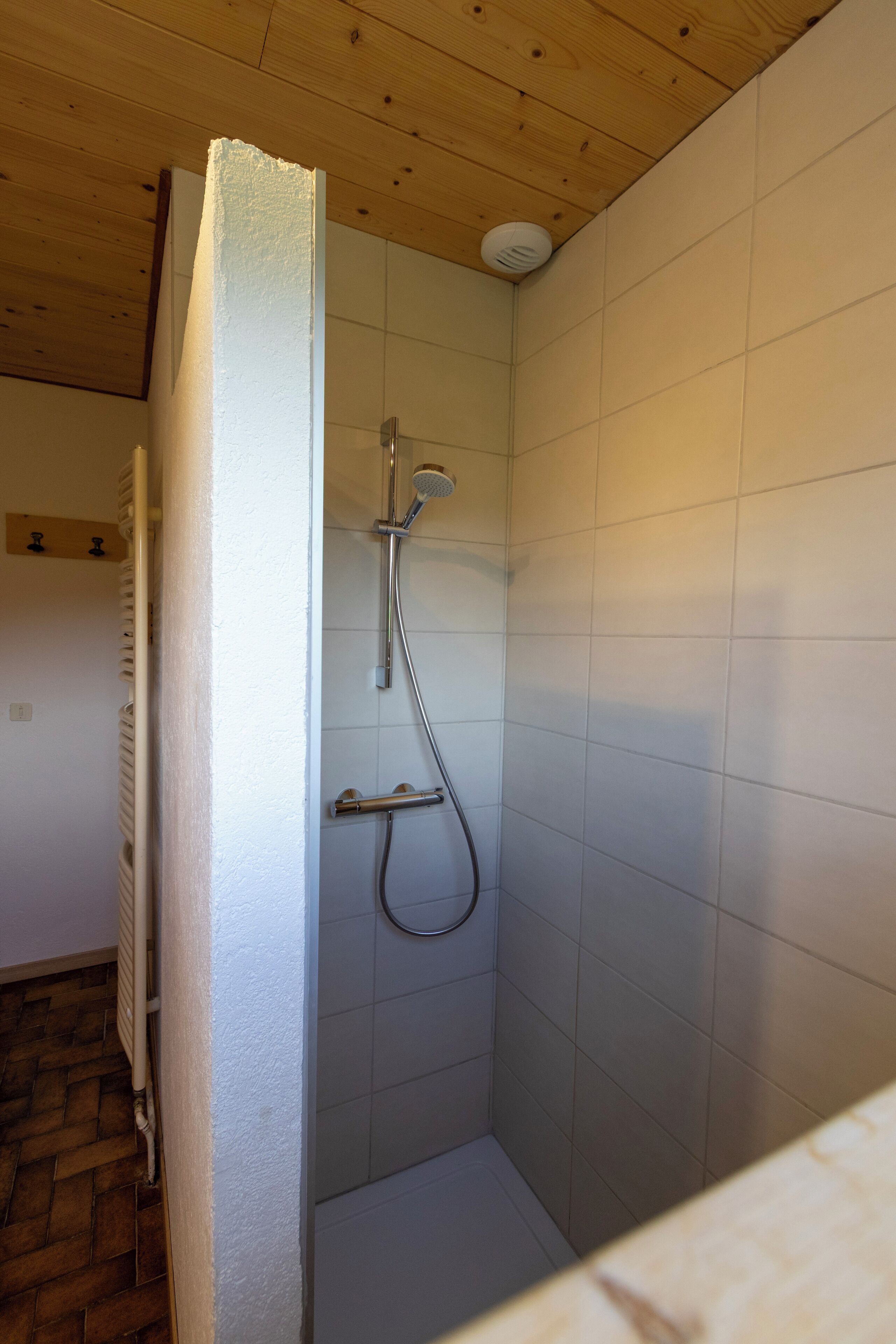 Een kleine, afgesloten douchecabine met een houten plafond en witte betegelde wanden.