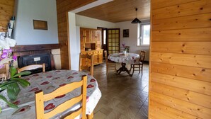 A wooden interior with a dining table, chairs, a fireplace, and a kitchen area. - Gîte 'La Pature', 2 to 6 persons (Le Barboux)