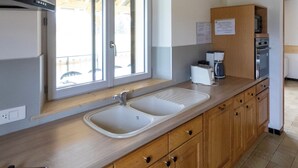 A kitchen with wooden cabinets, a double sink, and a window with blinds. - Gîte 'La Pature', 2 to 6 persons (Le Barboux)