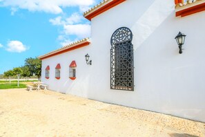 A white building with a tiled patio, a large decorative window, and two wall-mounted lanterns. - Montecristo 2 in Torrepalma (Carmona)