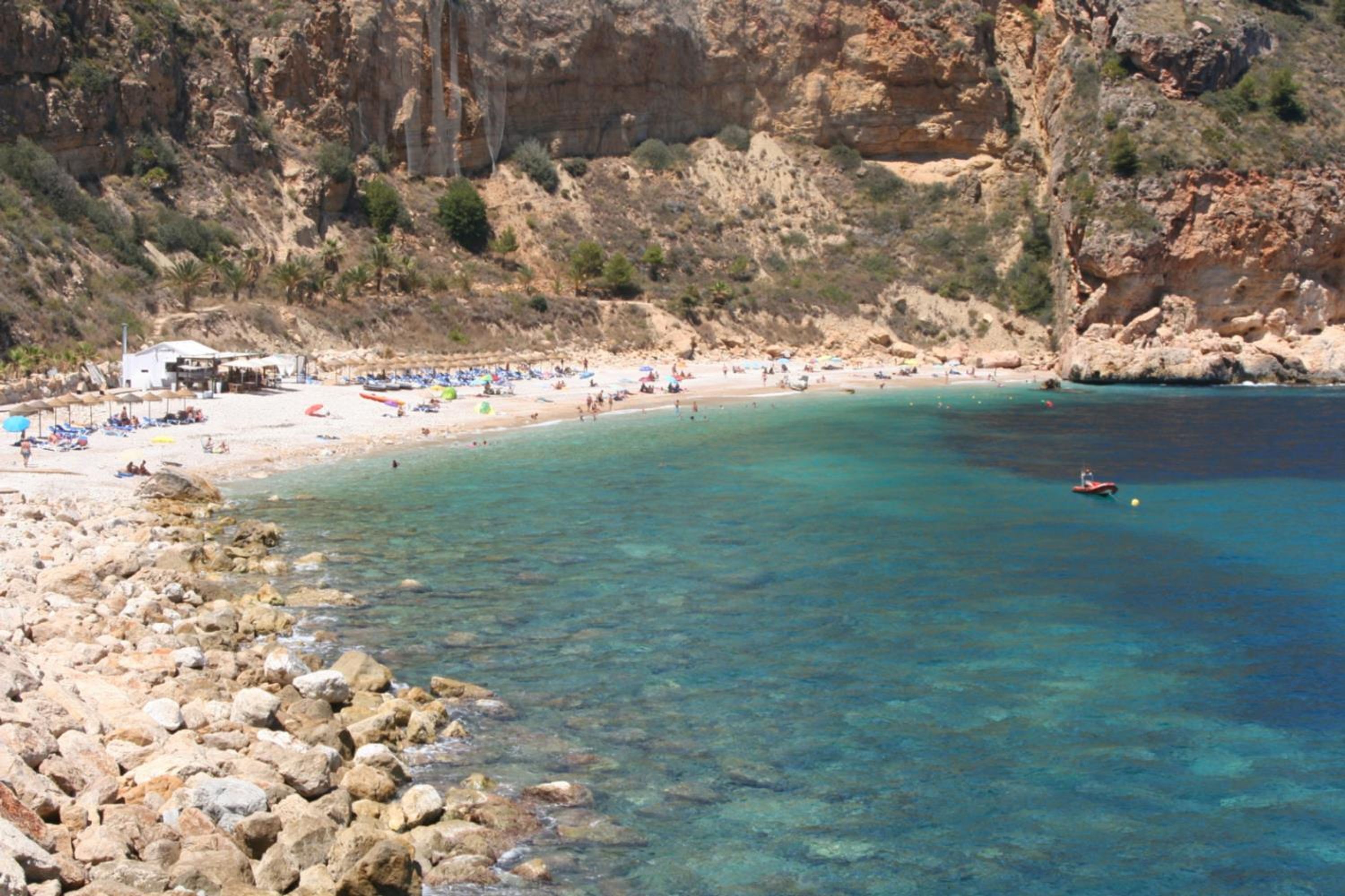 A rocky coastline with clear turquoise water, a sandy beach, and a small boat.