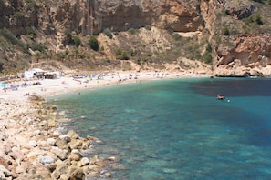 Eine felsige Küste mit klarem türkisblauem Wasser, einem Sandstrand und einem kleinen Boot.