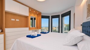Une chambre moderne avec un grand lit, une tête de lit en bois, une armoire intégrée et une vue sur la ville grâce à de grandes fenêtres.