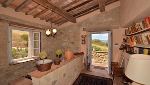 A rustic room with a stone wall, wooden beams, a bookshelf, a window with a view, and a small table with decorative items. - Casale Rigo in San Casciano dei Bagni (San Casciano dei Bagni)