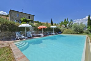 A swimming pool with lounge chairs and umbrellas, surrounded by stone walls and greenery. - Casale Rigo in San Casciano dei Bagni (San Casciano dei Bagni)
