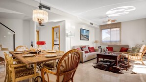 Amplia sala de estar con una mesa de comedor dispuesta para una comida, un sofá con cojines y una mesa de centro.