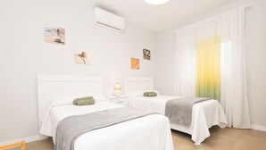 A hotel room with two beds, white bedding, a small bedside table with a lamp, and artwork on the walls. - Las Camelias in Chiclana de la Frontera (Chiclana de la Frontera)