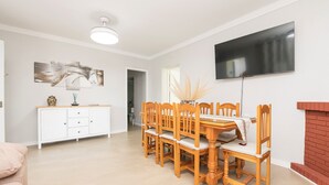A dining area with a wooden table and chairs, a white cabinet, a flat-screen TV mounted on the wall, and a fireplace. - Las Camelias in Chiclana de la Frontera (Chiclana de la Frontera)