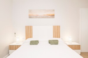 A modern bedroom with a large bed, two bedside tables with lamps, and a painting on the wall.
