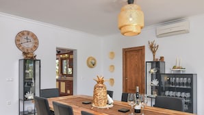Ein Esszimmer mit Holztisch, schwarzen Stühlen, einer großen Wanduhr und einer dekorativen Ananas als Mittelstück.