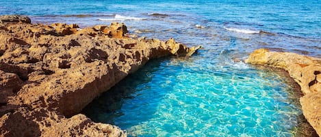 A rocky coastline with clear blue water and distant boats.