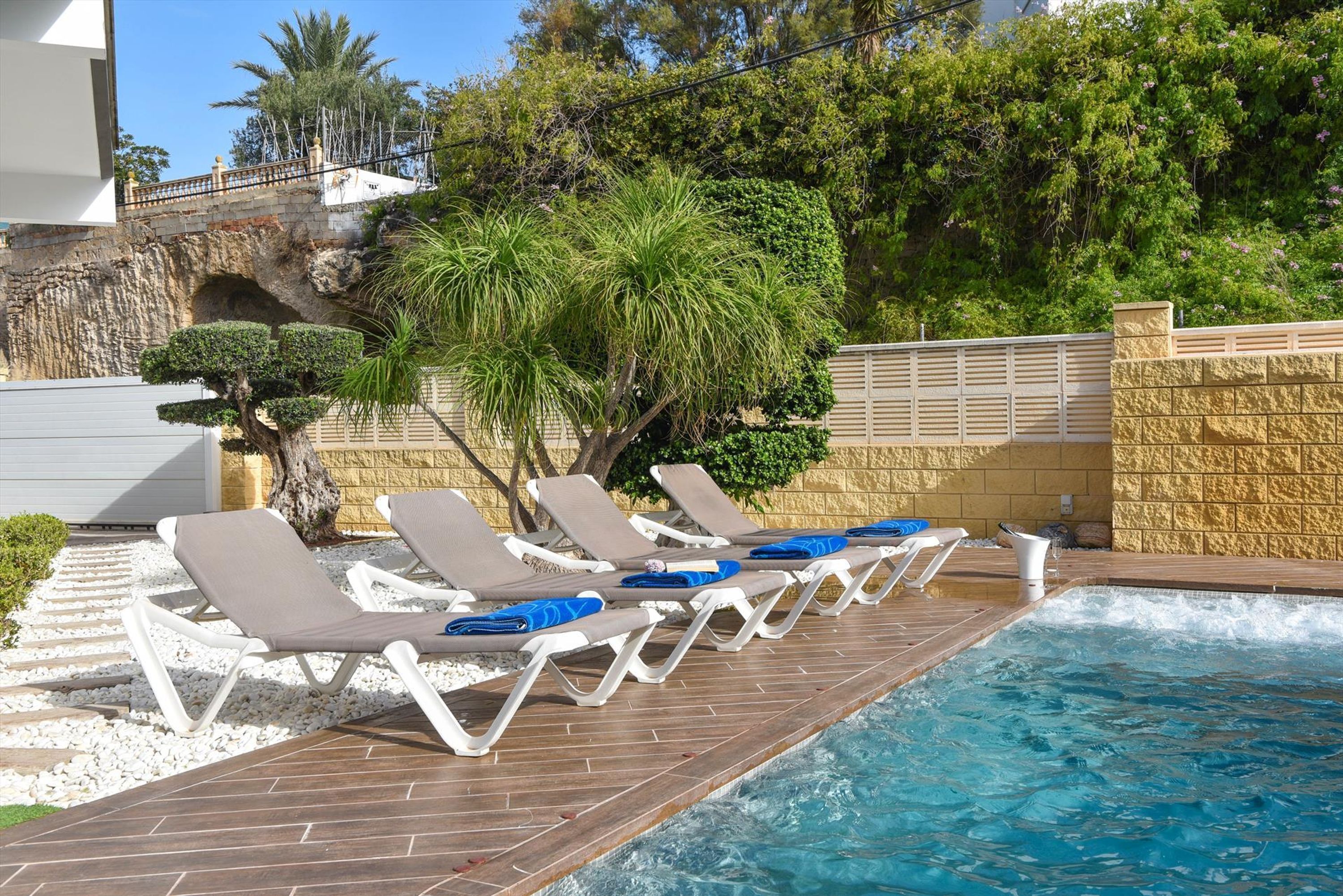 A pool area with lounge chairs and a stone wall.