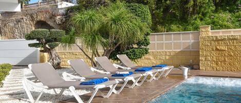 A pool area with lounge chairs and a stone wall.