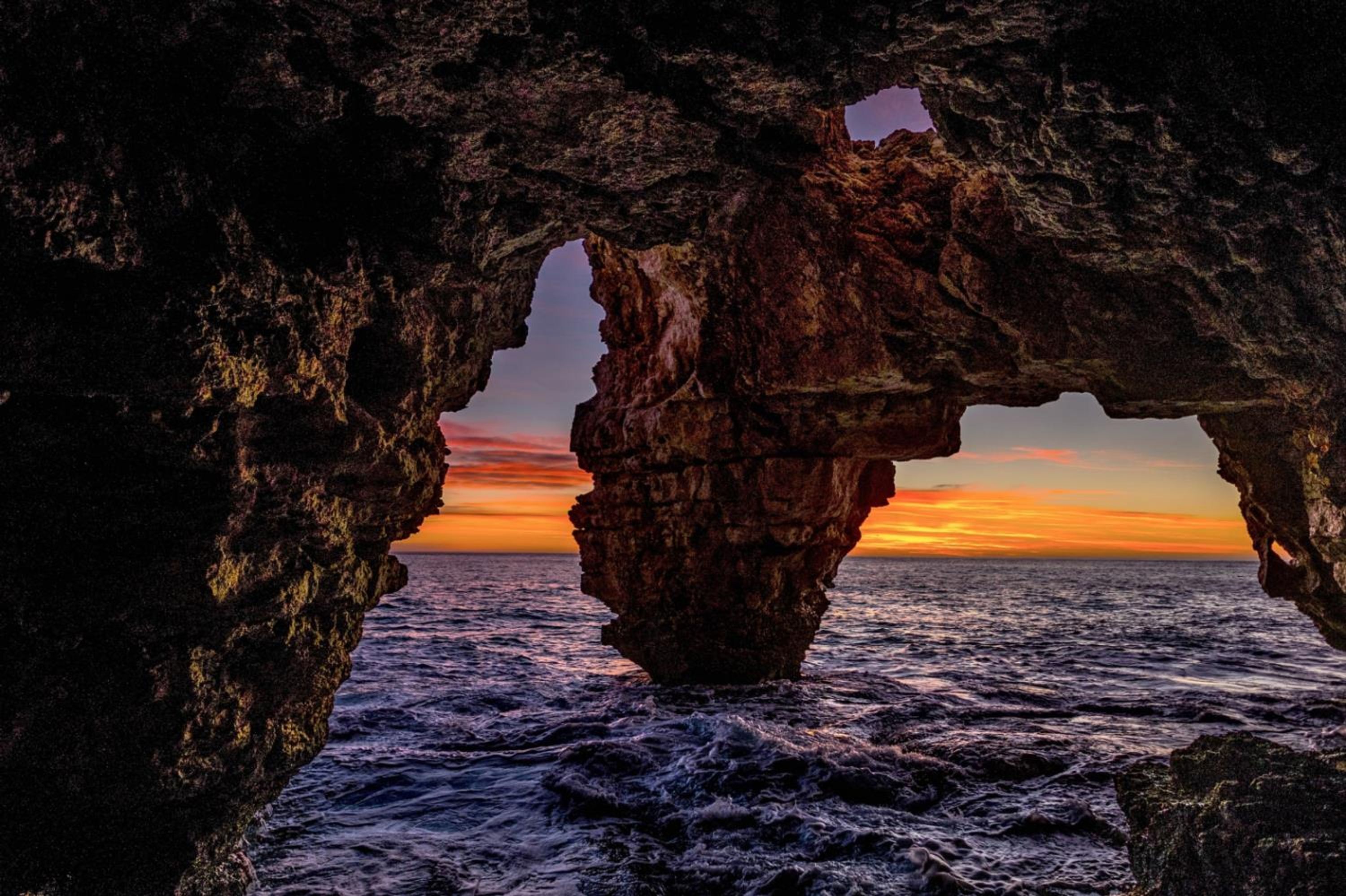 Une formation rocheuse naturelle avec une arche surplombant l’océan au coucher du soleil.